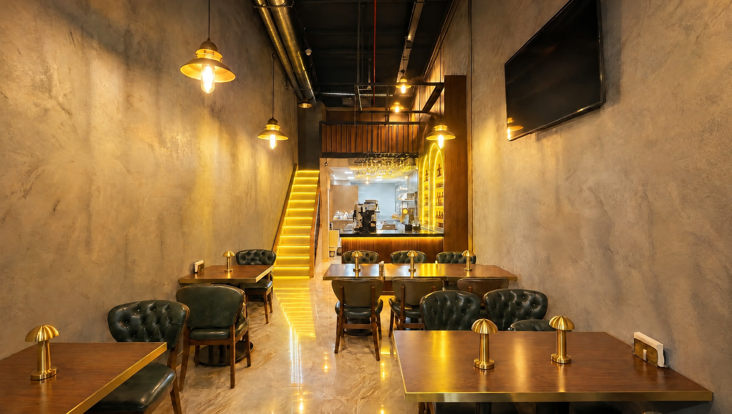 Spica Bistro salonu: ceviz masalar, pirinç masa lambaları, yeşil deri koltuklar ve arkada sarı ışıklı bar